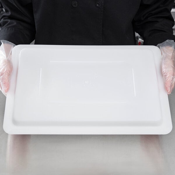 A person in gloves holding a white plastic Choice food storage box lid on a plastic tray.