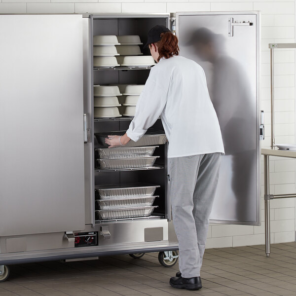 A person in a white coat opening a white door on a Metro heated banquet cabinet.