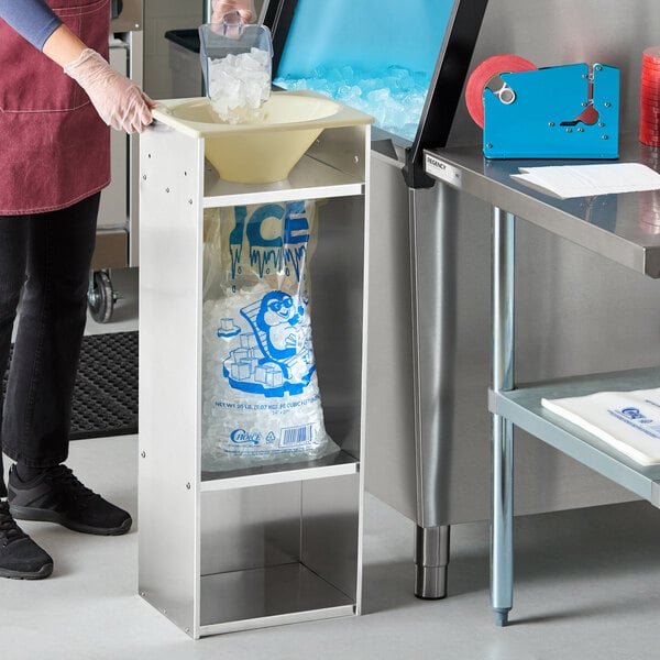 A stainless steel ice bagger starter kit with a yellow funnel and a 20 lb. ice bag positioned underneath.