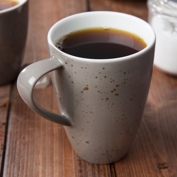 A close up of a Schonwald light gray porcelain mug with coffee on a wooden table.