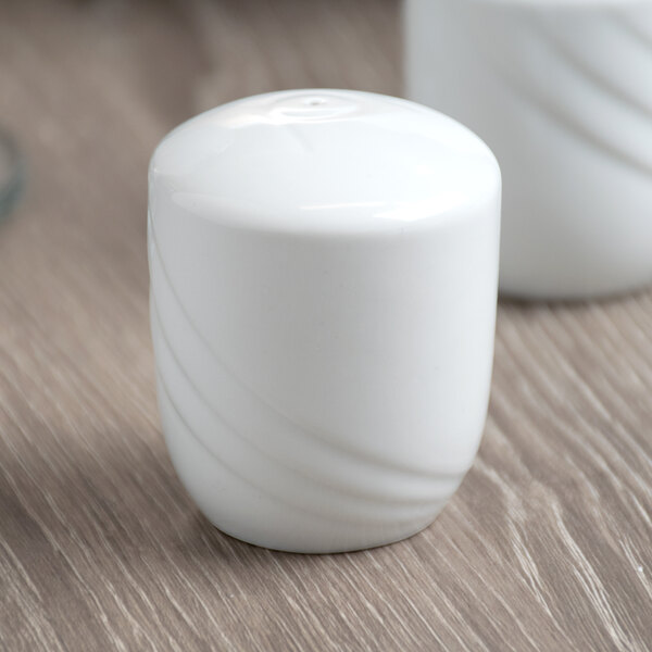 A Schonwald Donna white porcelain pepper shaker on a wood table.