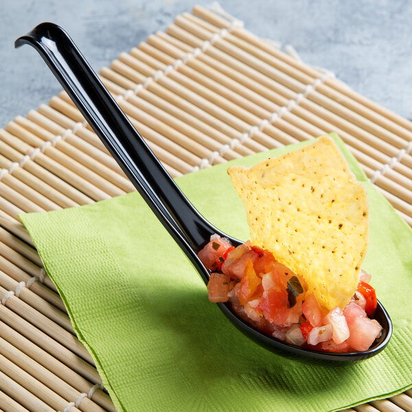 A Thunder Group black melamine Asian soup spoon filled with salsa with a tortilla chip on it.