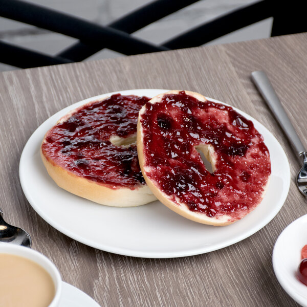 A Schonwald round white porcelain plate with a bagel and jam on it on a table with a cup of coffee.