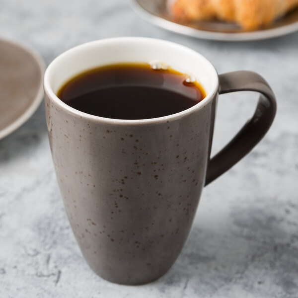 A dark gray Schonwald porcelain mug filled with coffee on a table.