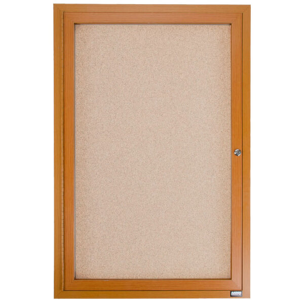 An Aarco enclosed bulletin board with a wooden frame and cork background behind a glass door.