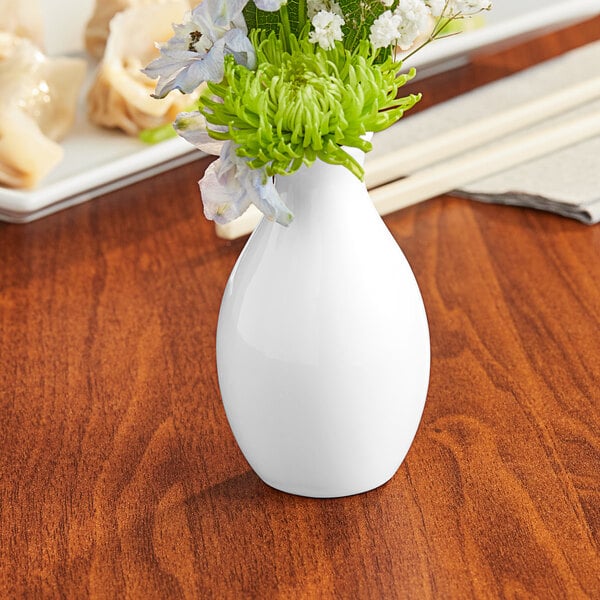 An Acopa bright white porcelain jug bud vase with flowers on a table.