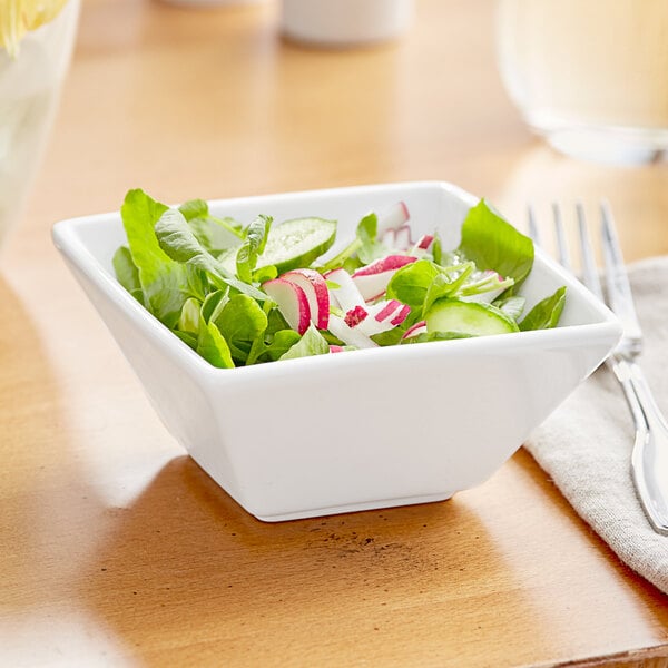 A bowl of salad with green leaves, radish, and cucumber in a white Acopa porcelain bowl.