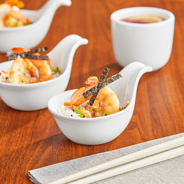Acopa white porcelain Asian soup spoons filled with shrimp and rice on a table with chopsticks.