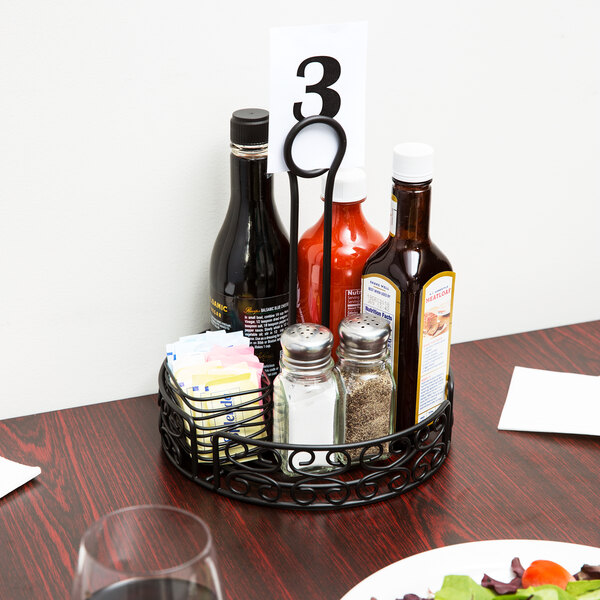 A black wrought iron condiment caddy on a table with condiments and salt shakers.
