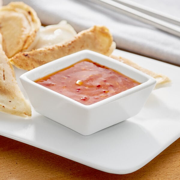 A plate of food with Acopa bright white porcelain sauce cup filled with red sauce on the side.