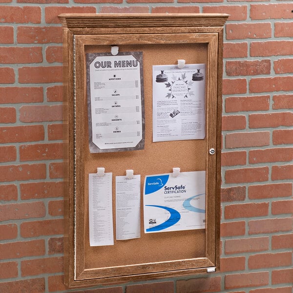 An Aarco natural oak enclosed bulletin board with cork papers attached.