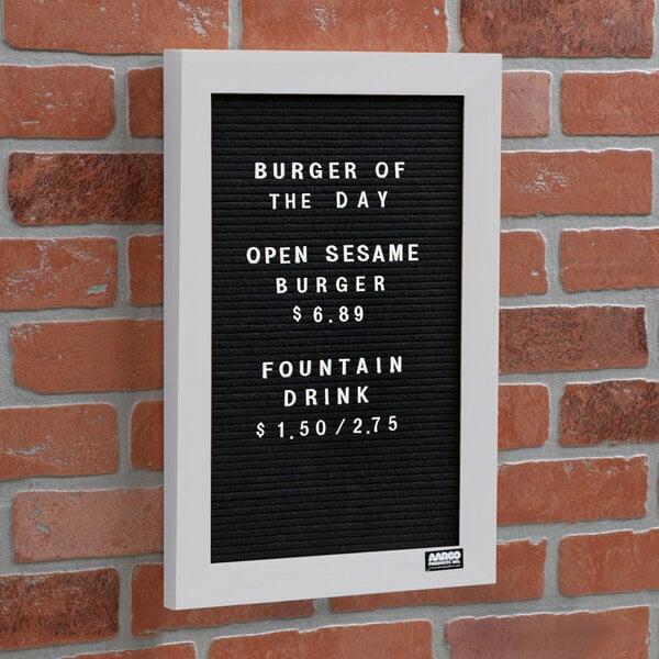 A black Aarco felt message board with white text that says "Burger of the Day" on a brick wall.
