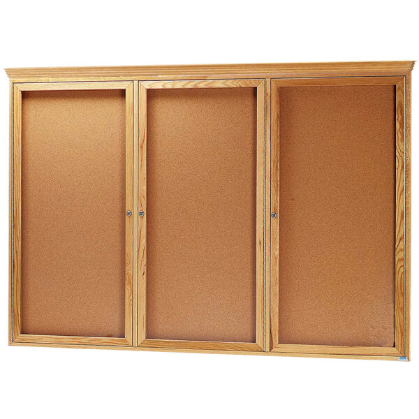 An Aarco natural oak enclosed bulletin board with 3 doors.