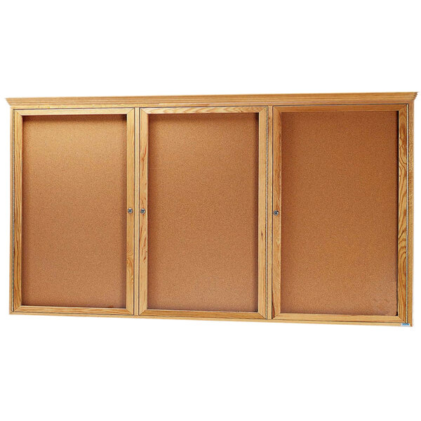 An Aarco natural oak enclosed bulletin board with three doors.