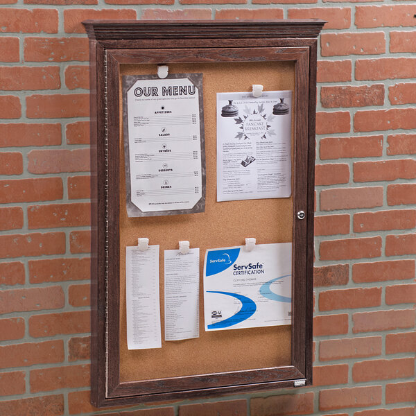 A wooden framed Aarco bulletin board with cork and papers attached.