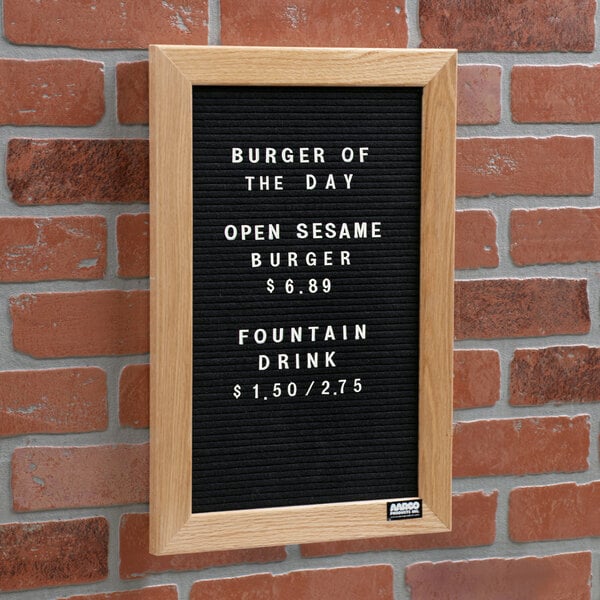 An Aarco black felt open face message board with white text that says "Burger of the Day" on a table in a farm-to-table restaurant.