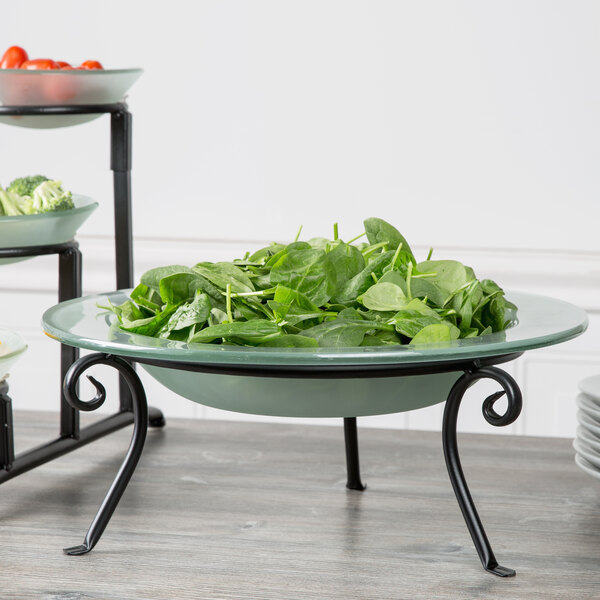 A bowl of greens sits on a Libbey round black metal display frame on a table.