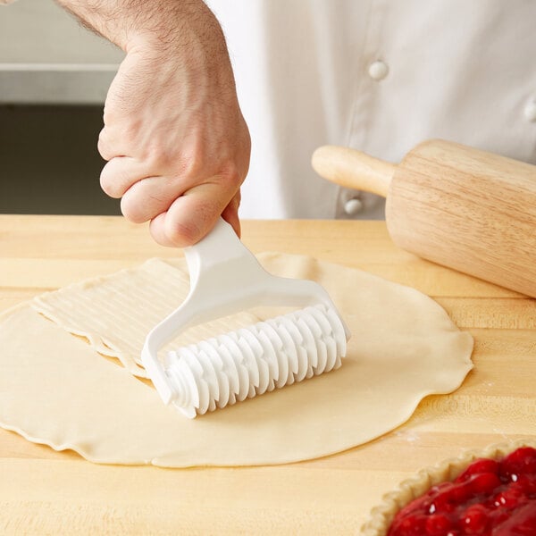 A hand using an Ateco lattice dough cutter to cut pie dough.