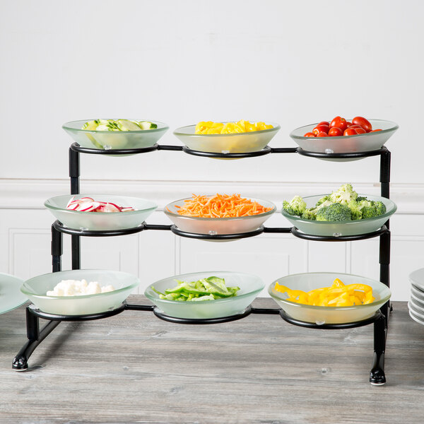 A Libbey black metal 3-tier banquet display frame with bowls of vegetables on it.