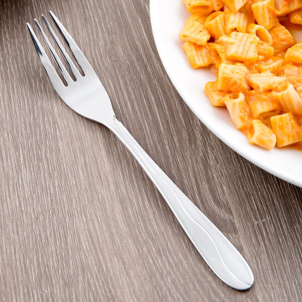 A Libbey stainless steel dessert fork next to a plate of pasta.