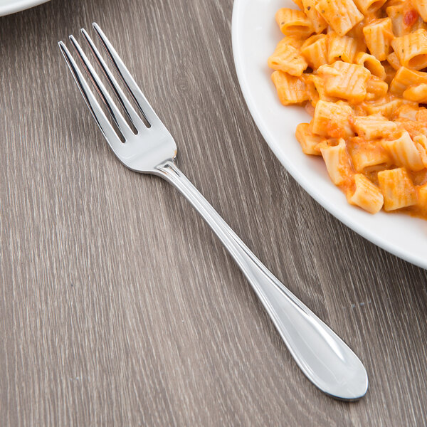 A Libbey stainless steel dinner fork next to a plate of pasta with sauce.
