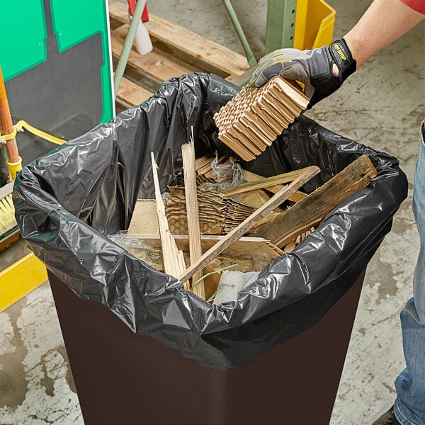 A man putting wood into a black trash can lined with a Lavex Pro heavy-duty garbage bag.