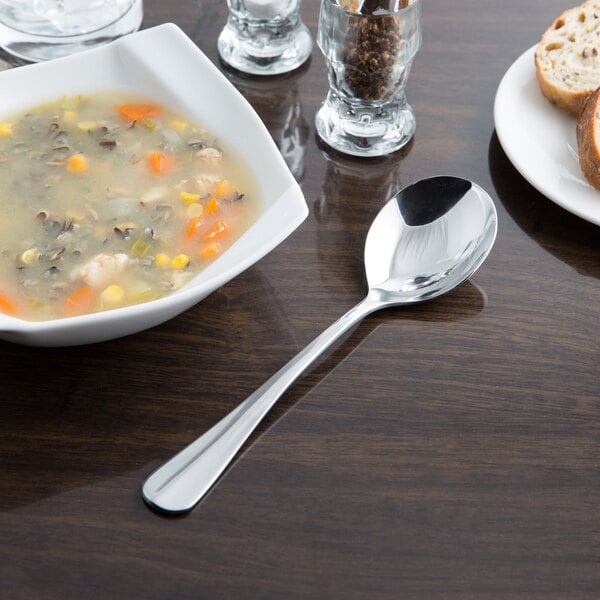 A bowl of soup next to a plate of bread with a Libbey stainless steel round soup spoon.