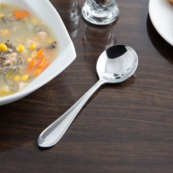 A bowl of soup with a Libbey stainless steel bouillon spoon on a table.