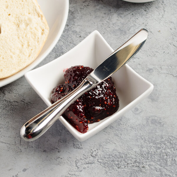 A bowl of jam with a knife next to a loaf of bread.