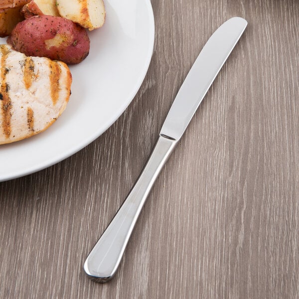 A Libbey stainless steel dinner knife on a table with a plate of grilled chicken and potatoes.
