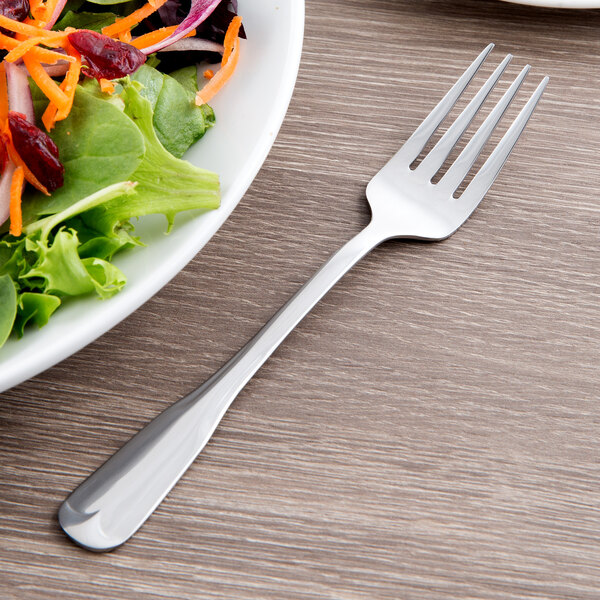 A World Tableware stainless steel salad fork next to a plate of salad.