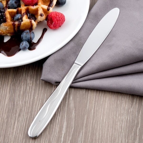 A Libbey stainless steel fluted utility knife on a plate of waffles with berries and chocolate sauce.