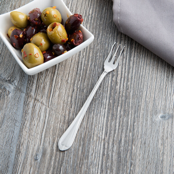 A bowl of green olives with a silver Libbey cocktail fork on a wood surface.