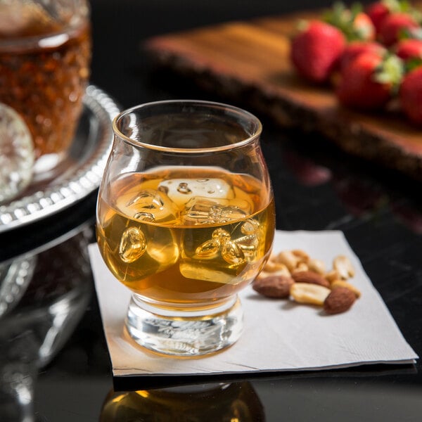 A Reserve by Libbey Kentucky Bourbon Trail Tasting Glass filled with bourbon and ice with nuts on a napkin on a table.