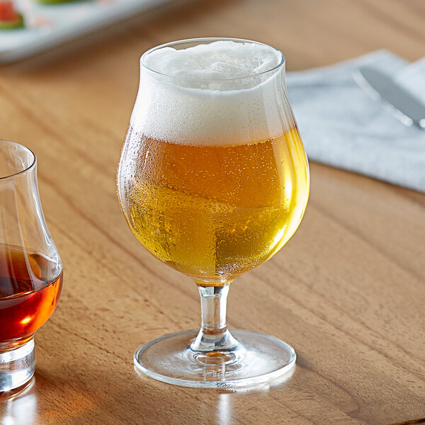 A Libbey Belgian beer glass filled with beer alongside an empty Libbey Belgian beer glass.