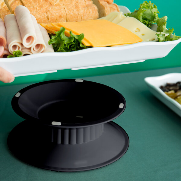 A black bowl on a white dotted melamine pedestal holding a plate of food.