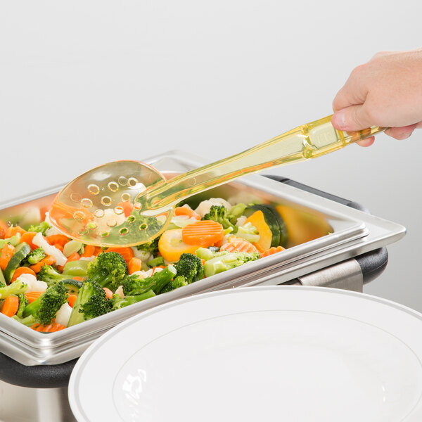 A person uses a Cambro amber perforated spoon at a salad bar to serve vegetables.