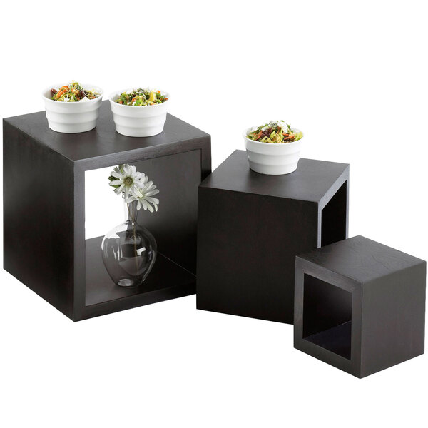 Three black wooden cube risers with bowls of food on top.