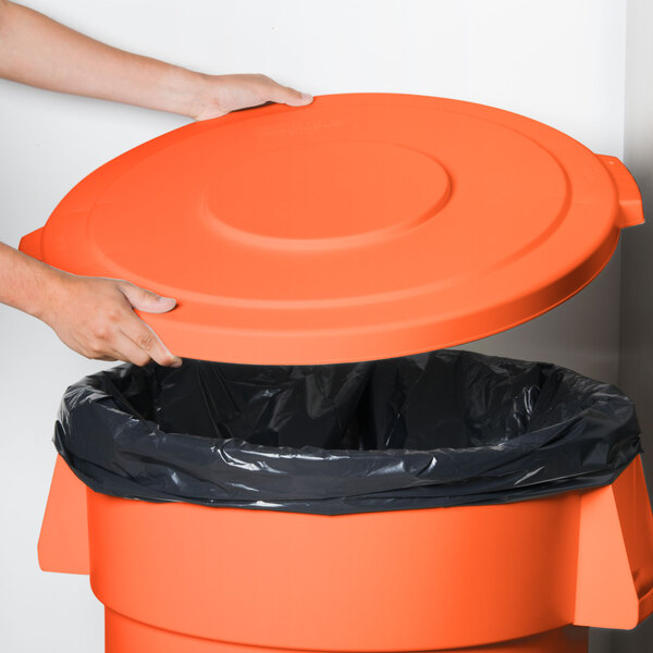 A person placing an orange Carlisle Bronco trash can lid on a trash can.