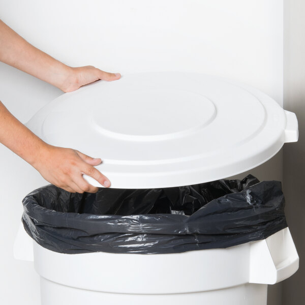 A person's hands placing a black bag in a Carlisle white trash can lid.