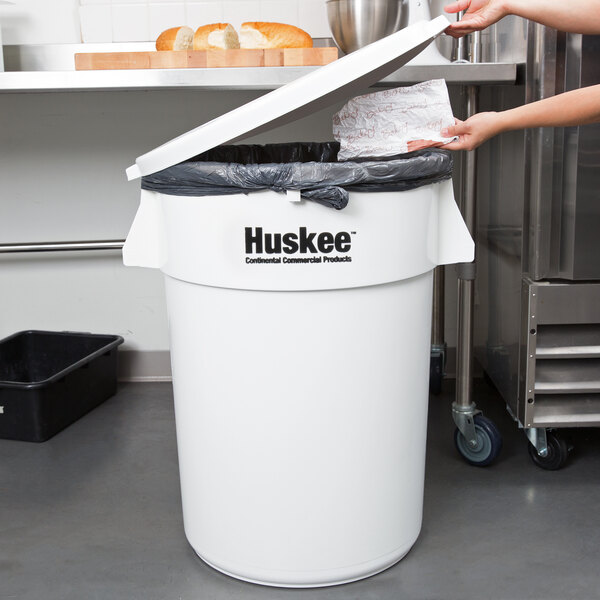 A woman putting a black plastic bag in a white Continental Huskee round trash can.