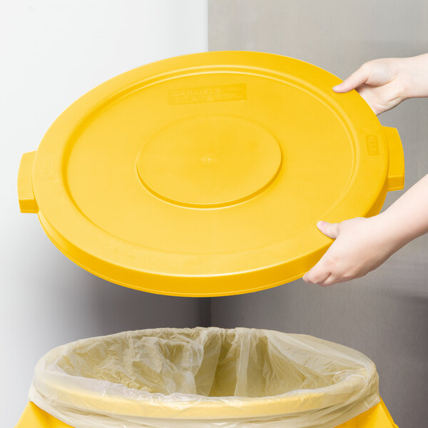 A person placing a yellow Carlisle Bronco lid on a yellow trash can.