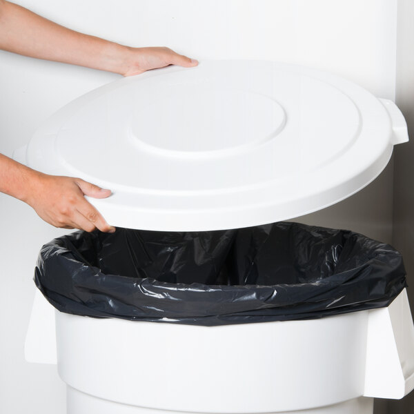 A person's hand opening a Carlisle white flat round trash can lid.