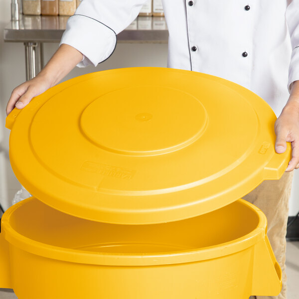 A person holding a Carlisle yellow flat round trash can lid.