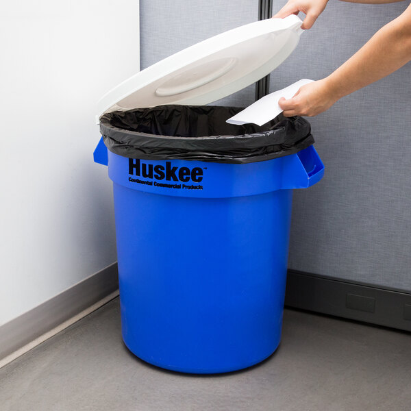 A woman putting a paper into a blue recycling can.