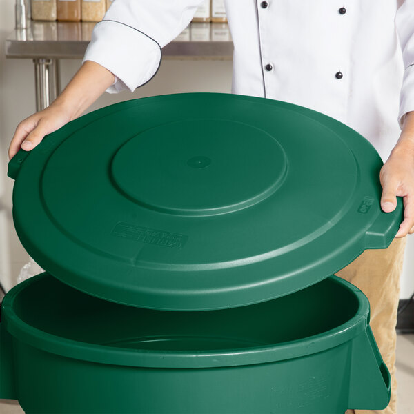 A person holding a Carlisle green round trash can lid.