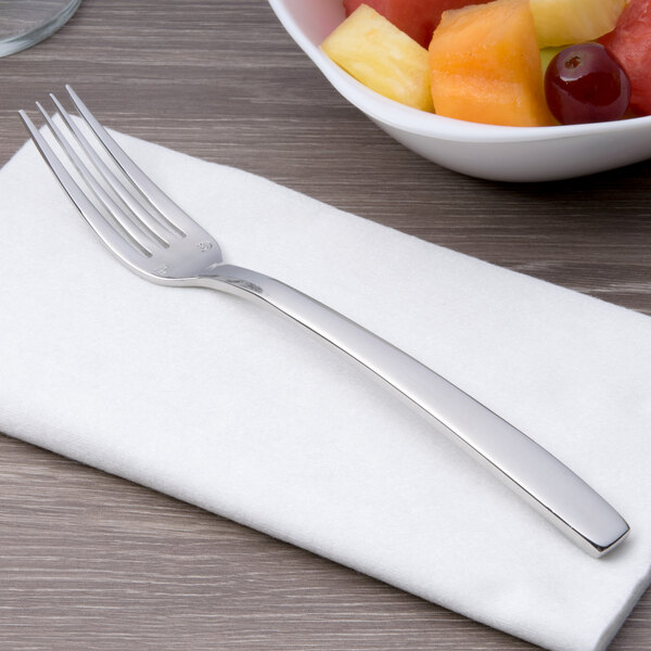 A Chef & Sommelier stainless steel dessert fork on a napkin next to a bowl of fruit.