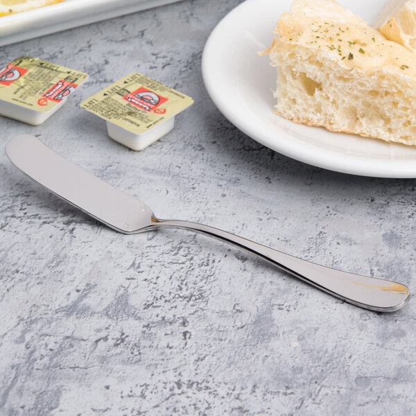 A silver butter knife on a table with a plate of butter and a piece of bread.