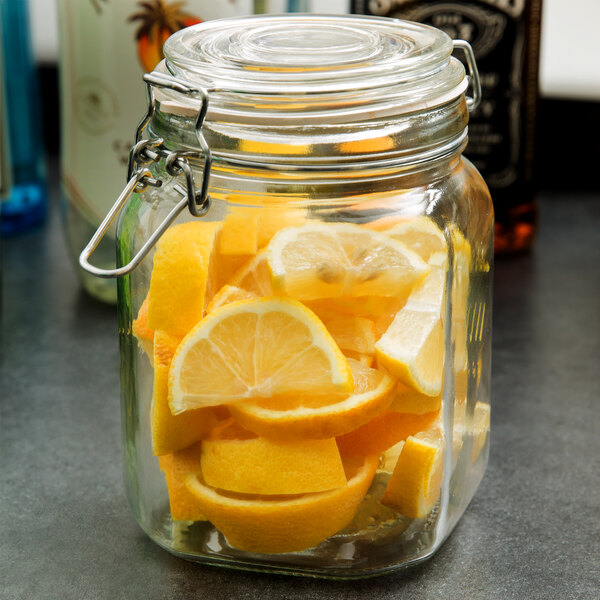 An Anchor Hocking Hermes jar filled with lemons, lemon slices, and oranges on a counter.