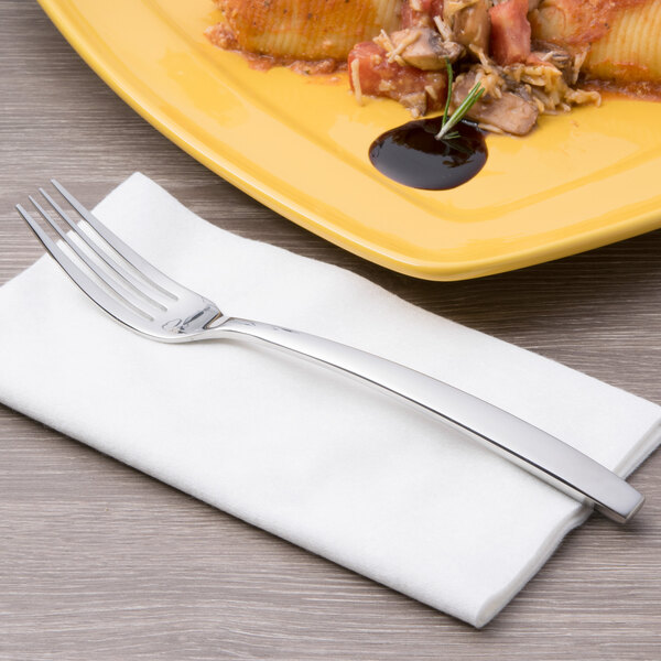 A Chef & Sommelier stainless steel dinner fork on a white napkin next to a plate of pasta.